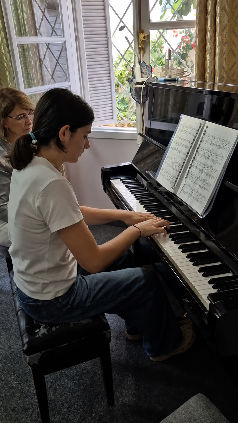 Élève au piano, partition ouverte, accompagnée par sa professeure