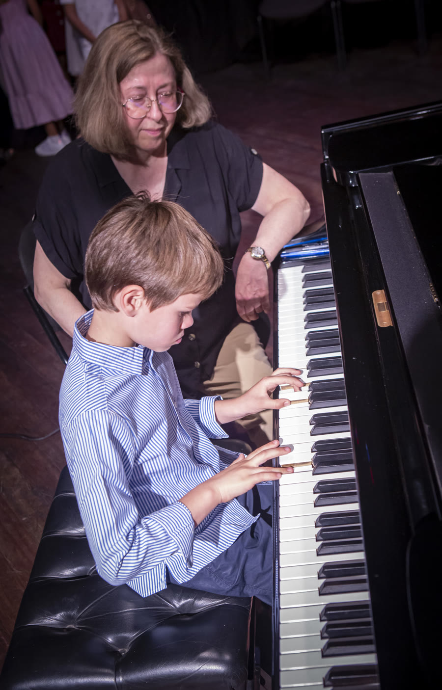 Jeune élève au piano à queue, accompagné par sa professeure